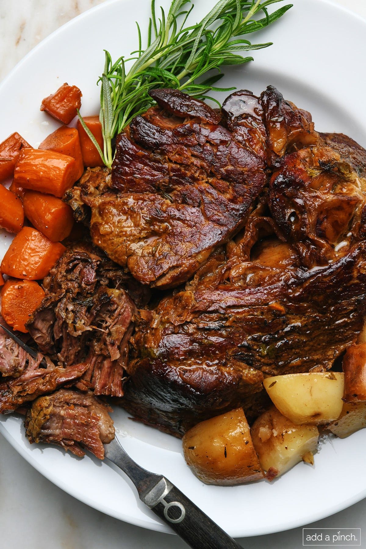 Serving platter filled with pot roast, carrots, potatoes, celery, onion, and herbs.