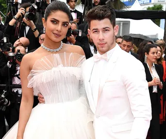 A couple dressed elegantly, posing on the red carpet with photographers in the background.