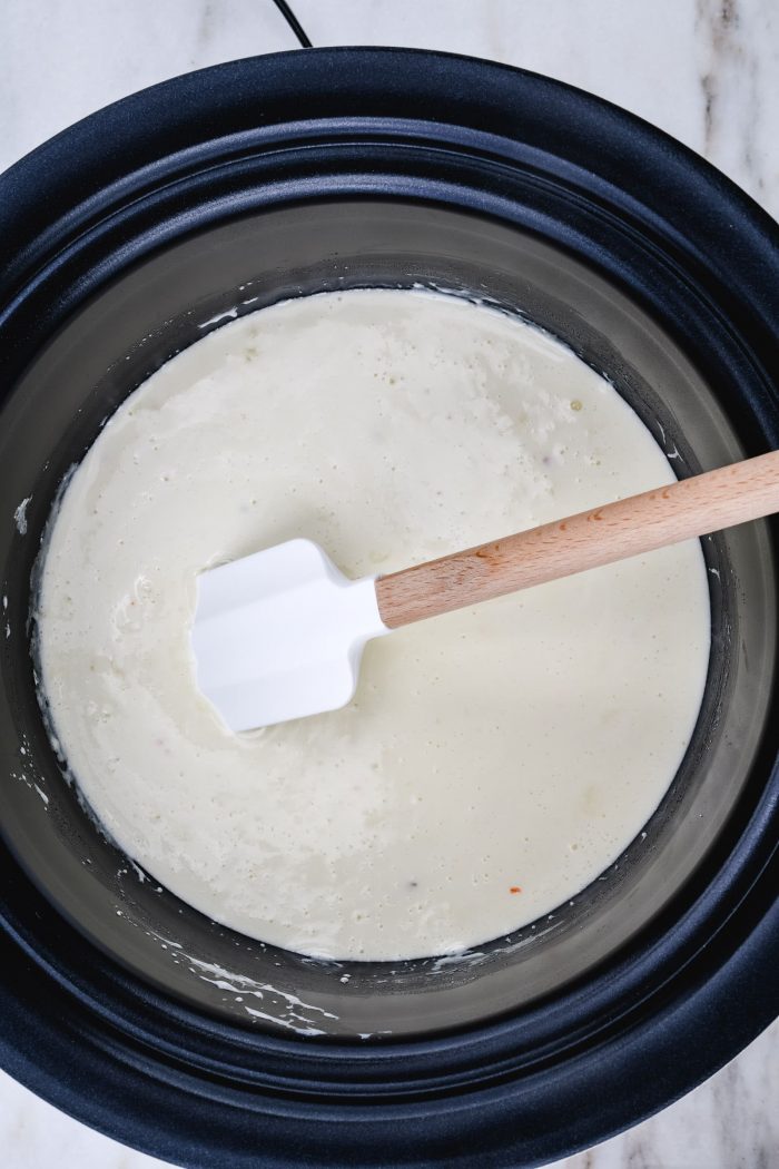 Melted cheeses stirred with a spatula  in a slow cooker insert. 