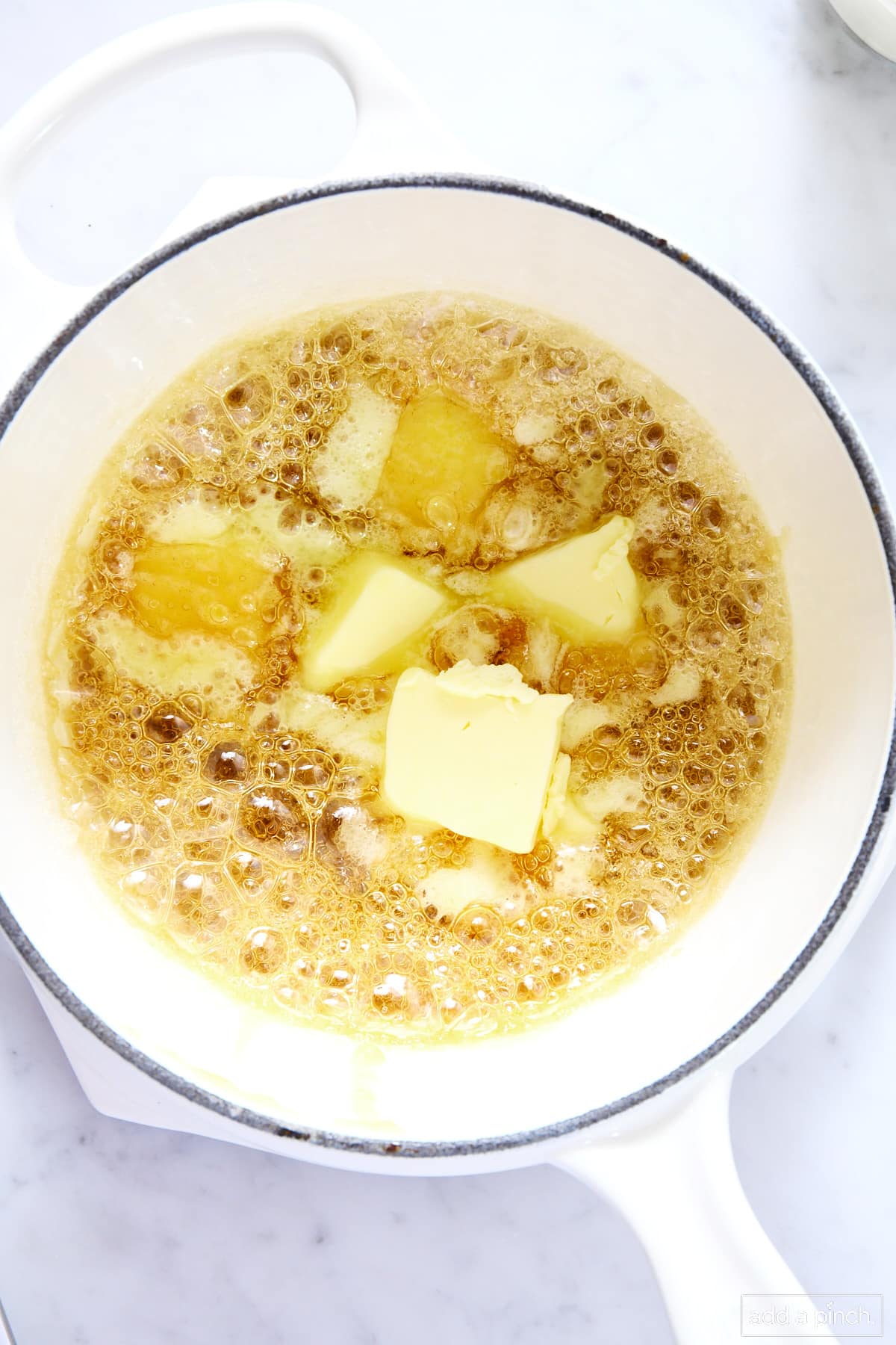 Butter added to caramel sauce in a white saucepan on a marble surface.