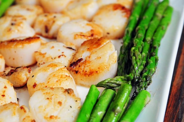 Horizontal photograph of cooked scallops and asparagus on a white plate. // addapinch.com