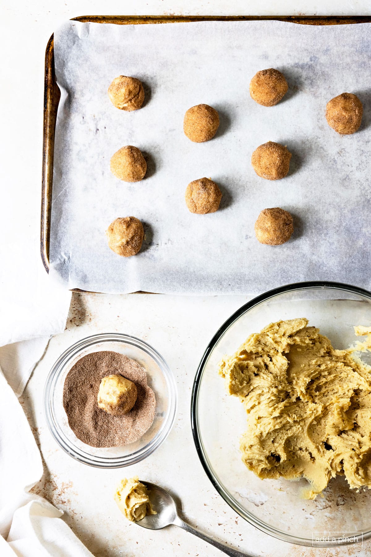 Photograph of the making of snickerdoodles with dough in a glass bowl, rolling cookies in cinnamon sugar mixture, and placing on a baking sheet.