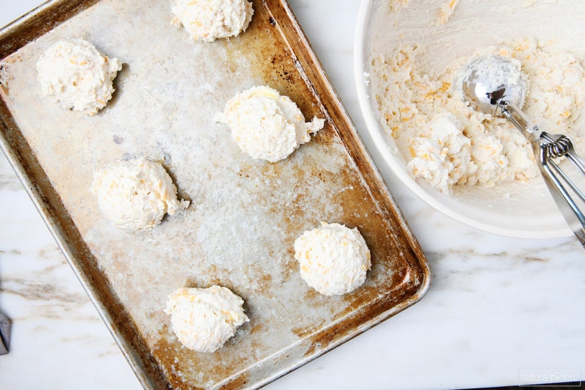 Cheddar biscuit dough dropped with scoop onto baking sheet.