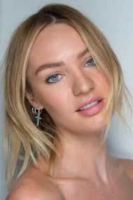 A woman with blonde hair and blue eyes wears a turquoise earring and smiles slightly against a neutral background.