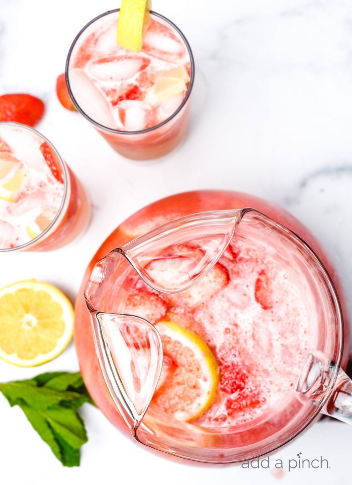 Top view of pitcher of garnished strawberry lemonade surrounded by lemon slices, glasses and mint sprigs  // addapinch.com