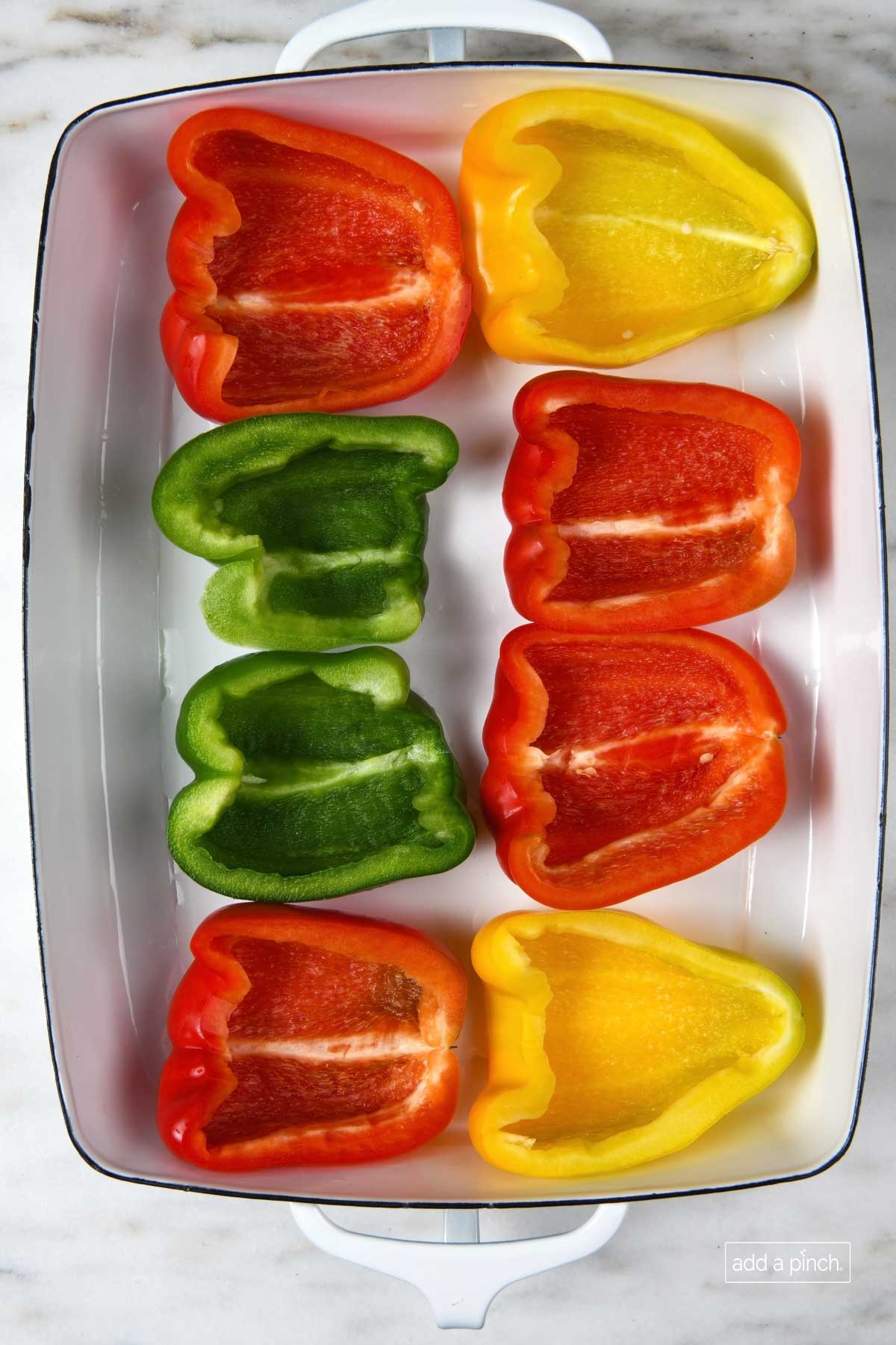 Red, yellow and green bell peppers cut lengthwise with the seeds and membrane removed in a baking dish.