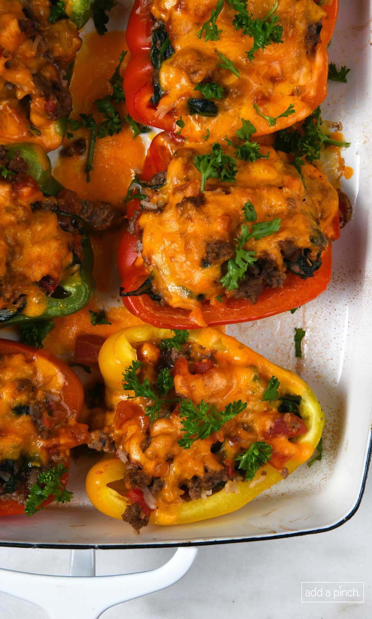 Red, yellow and green peppers stuffed with beef and topped in melted cheese in a white baking dish.