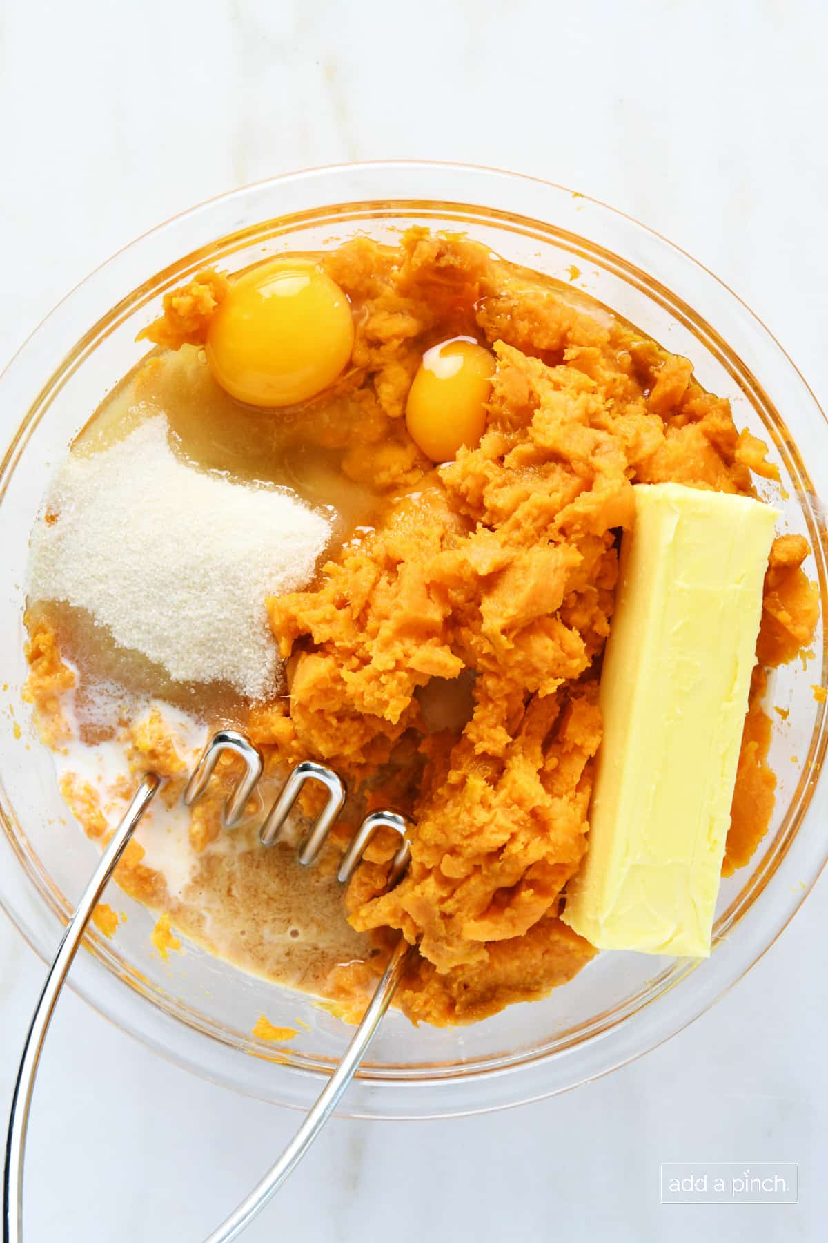 Ingredients for sweet potato casserole filling in a glass mixing bowl with a potato masher.