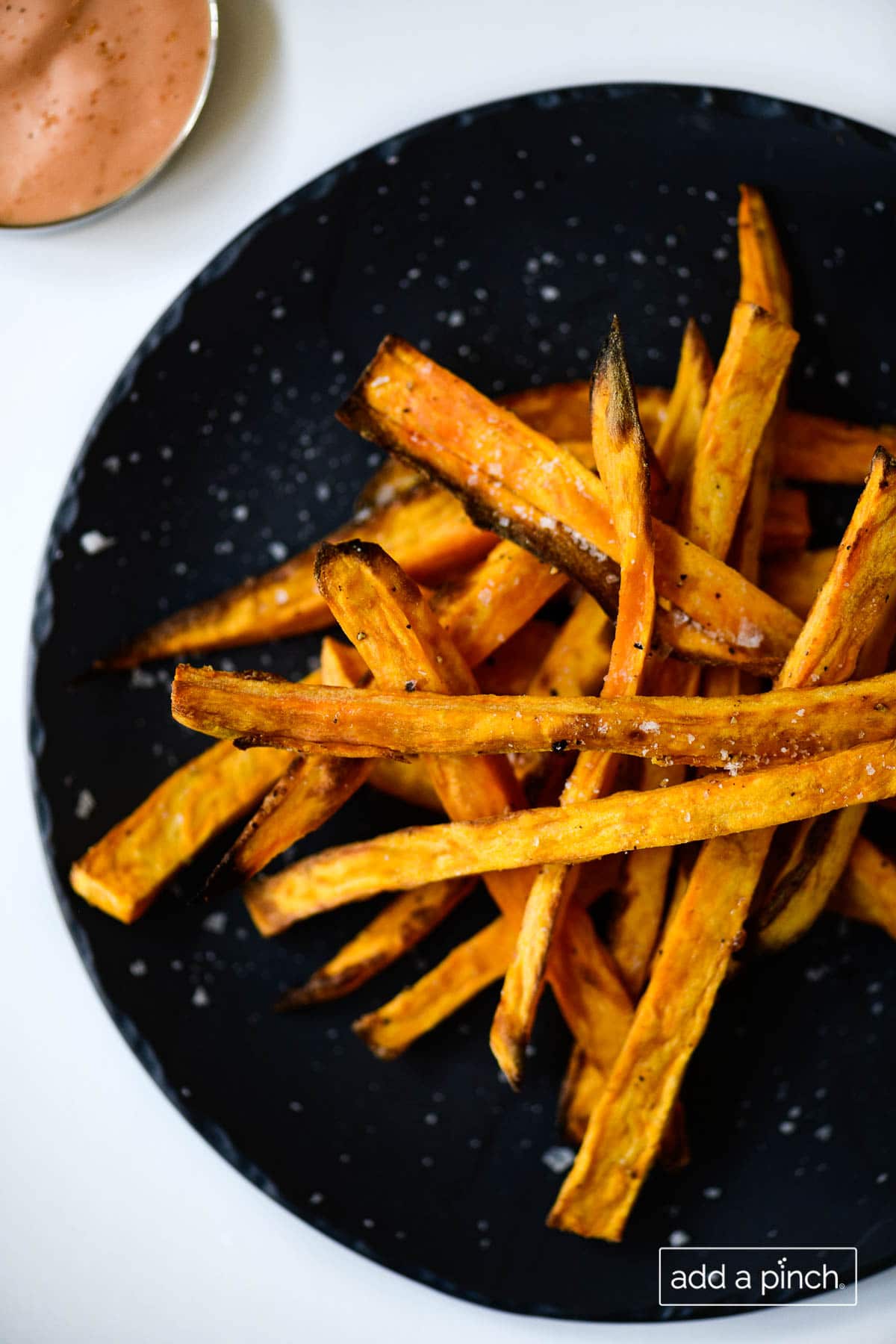 Photograph of sweet potato fries on a black plate on a white background. 