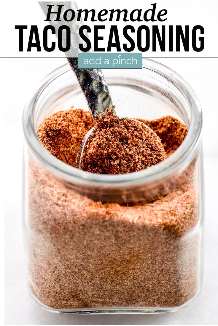 Homemade Taco Seasoning in a glass jar, scooped with a measuring spoon - with text - addapinch.com