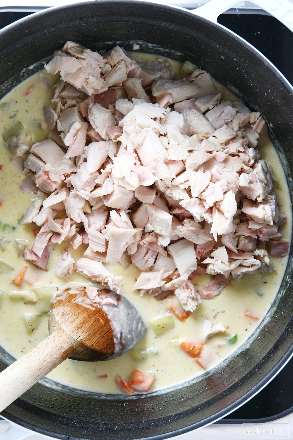 Chopped turkey being added to turkey pot pie filling in a Dutch oven.