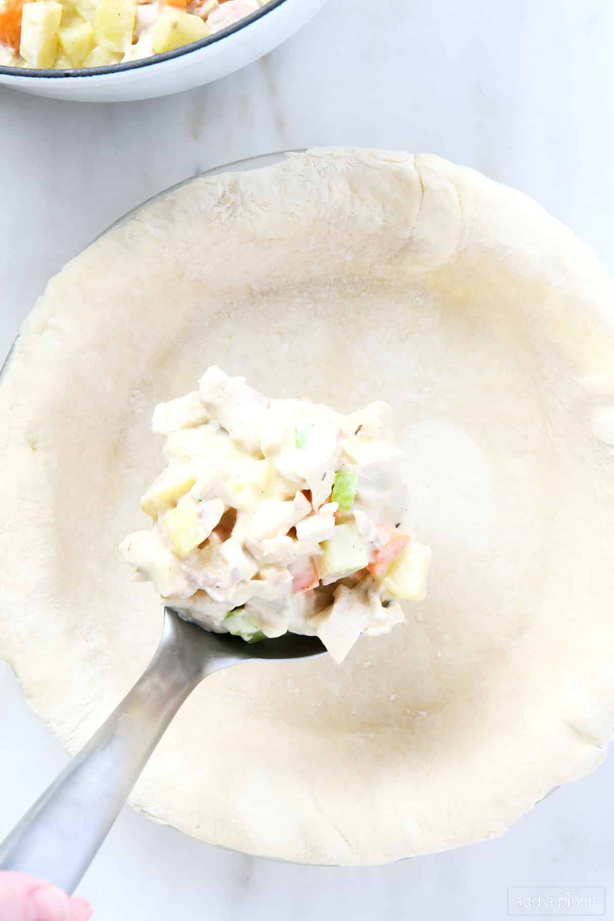 Ladle filled with turkey pot pie filling being added to pie crust.