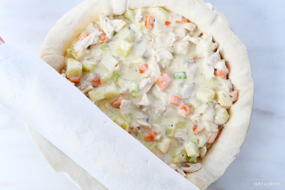 Top crust being rolled onto the top of turkey pot pie.