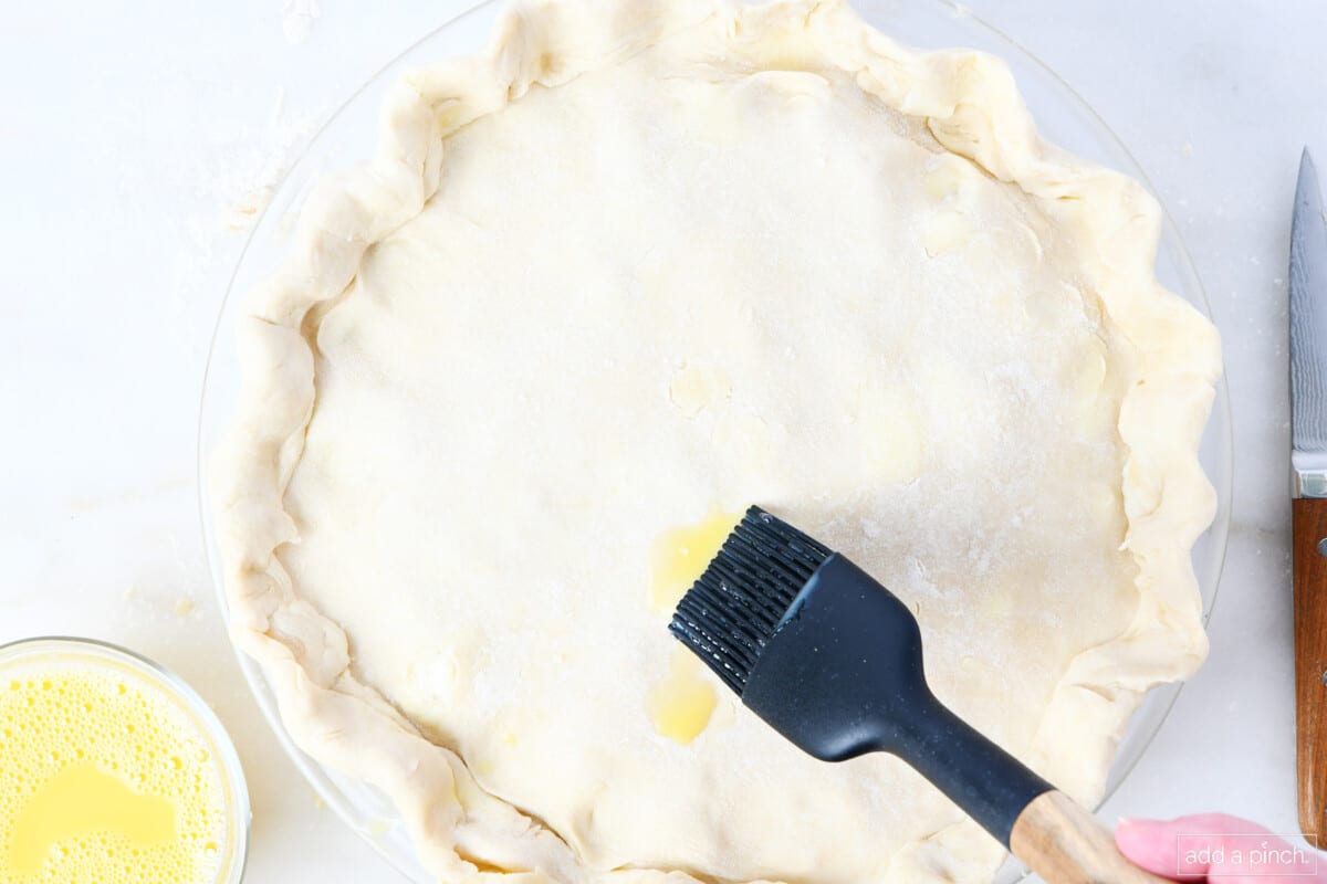 Brushing egg wash onto the top of turkey pot pie.