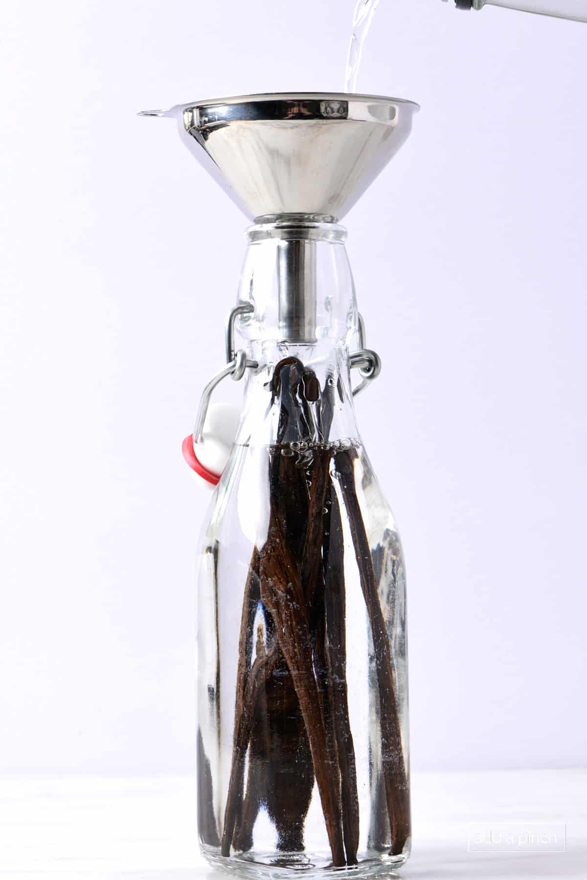 Vanilla beans in a swing top jar with funnel and pouring vodka into the bottle to make vanilla extract.