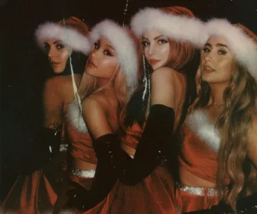 Four women in Santa costumes and hats pose closely together, reminiscent of "Mean Girls" Christmas scene.