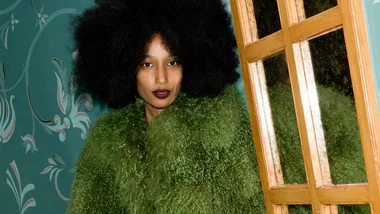 Woman with black curly hair wearing a green fur jacket